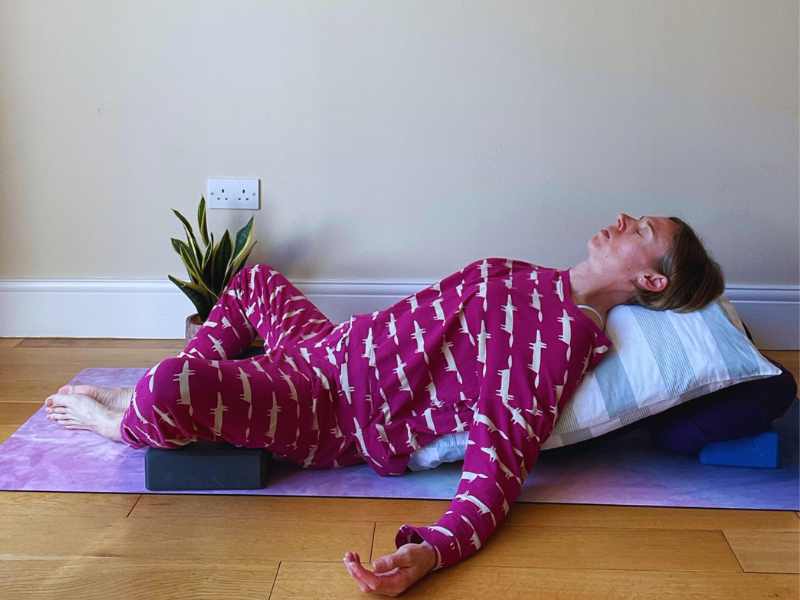 female yoga teacher lying back in reclined bound angle pose with lots of supports
