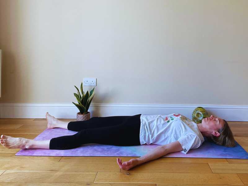 female yoga teacher laying down on mat in savasana