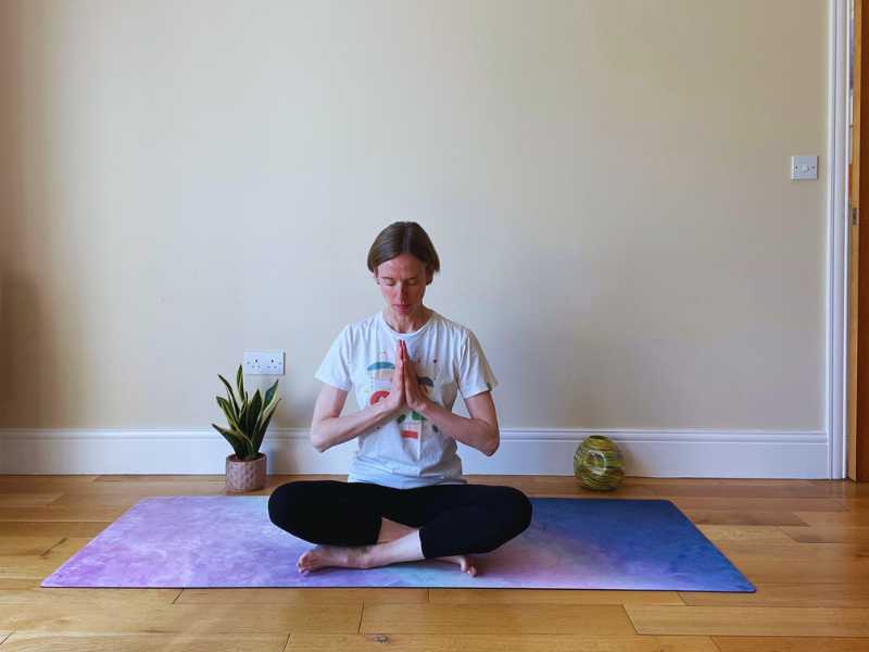 female yoga teacher seated on mat with hands at heart centre 