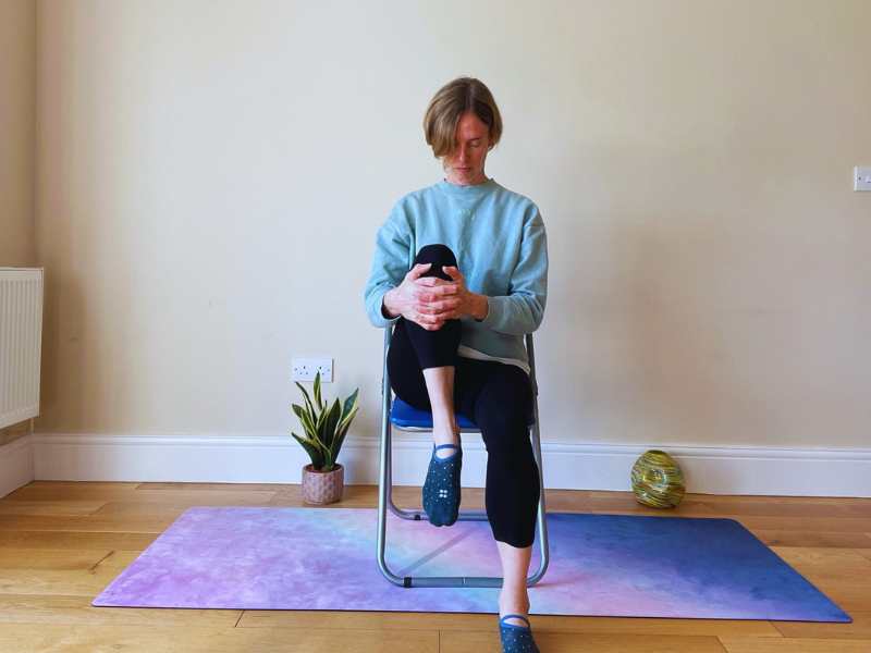 Female yoga teacher doing knee to chest pose on a chair
