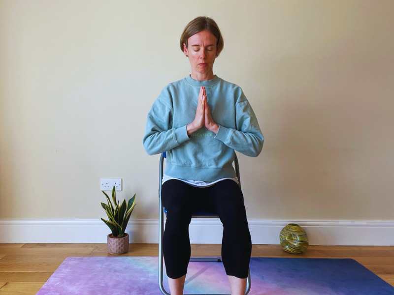 Female yoga sat on a chair with hands to heart centre